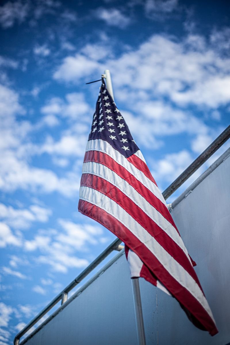 United States flag on a pole against a bright blue sky with clouds.